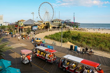 North Beach section of Boardwalk in Atlantic City with boardwalk trams and rolling chair,  Steel Pier and Landshark Bar and Grill at Resorts in view.
