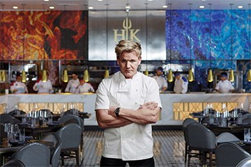Gordon Ramsey stands looking stern inside a Hell's Kitchen restaurant interior.
