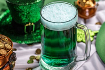 Green beer in a mug with pot of gold and green top hat.
