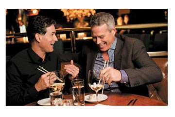 Two men laughing enjoying some casual dining eating with chopsticks.
