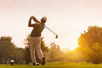 Golfer swinging into the sun with trees and course in view.