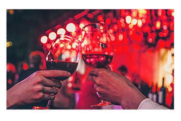People toasting hands visible holding wine glasses with red wine and red lighting in background