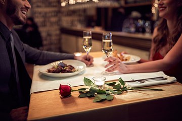 couple sharing a laugh over dinner and wine. Rose on table.