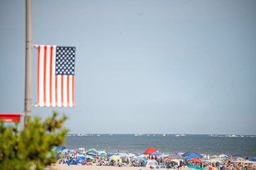 American Flag attached to a light post with beach goers and ocean in view.