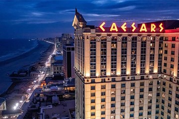Caesars Atlantic City tower with lit up sign and beach and boardwalk at night.