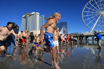 People in bathing suits run along the shoreline of the Atlantic City Beach into the cold waters on New Year's Day. Steel Pier and Casinos in background.