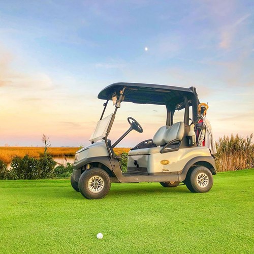 Golf Cart with clubs on a golf course near wetlands around sunset with moon visible.
