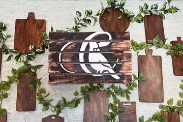 Cardinal Restaurant cutting boards and logo on wall with greenery